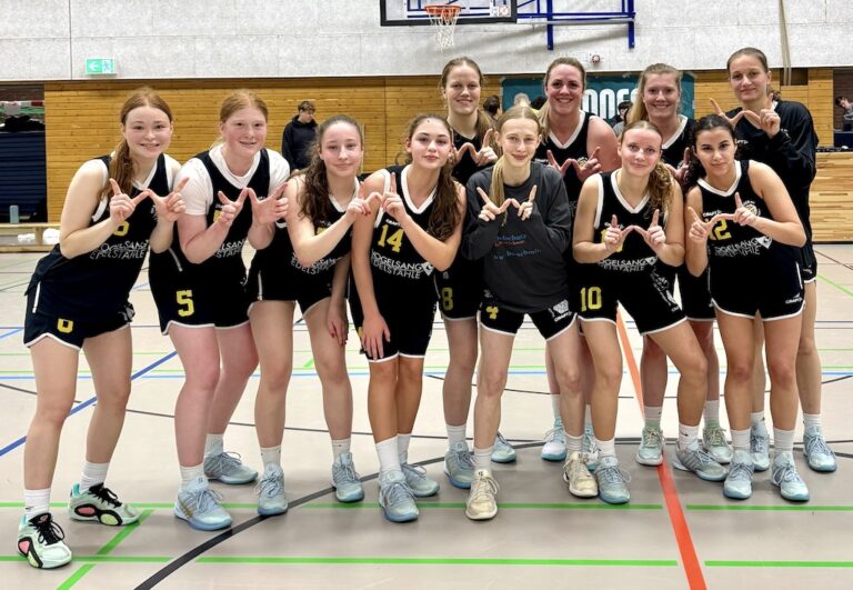 Laechelndes Basketballteam in schwarzen Trikots formt Handzeichen in der Halle