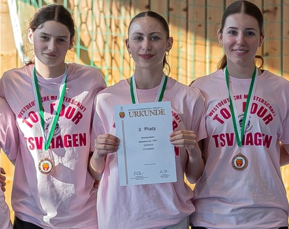 Drei laechelnde junge Frauen in rosa Shirts mit Medaillen und Urkunde