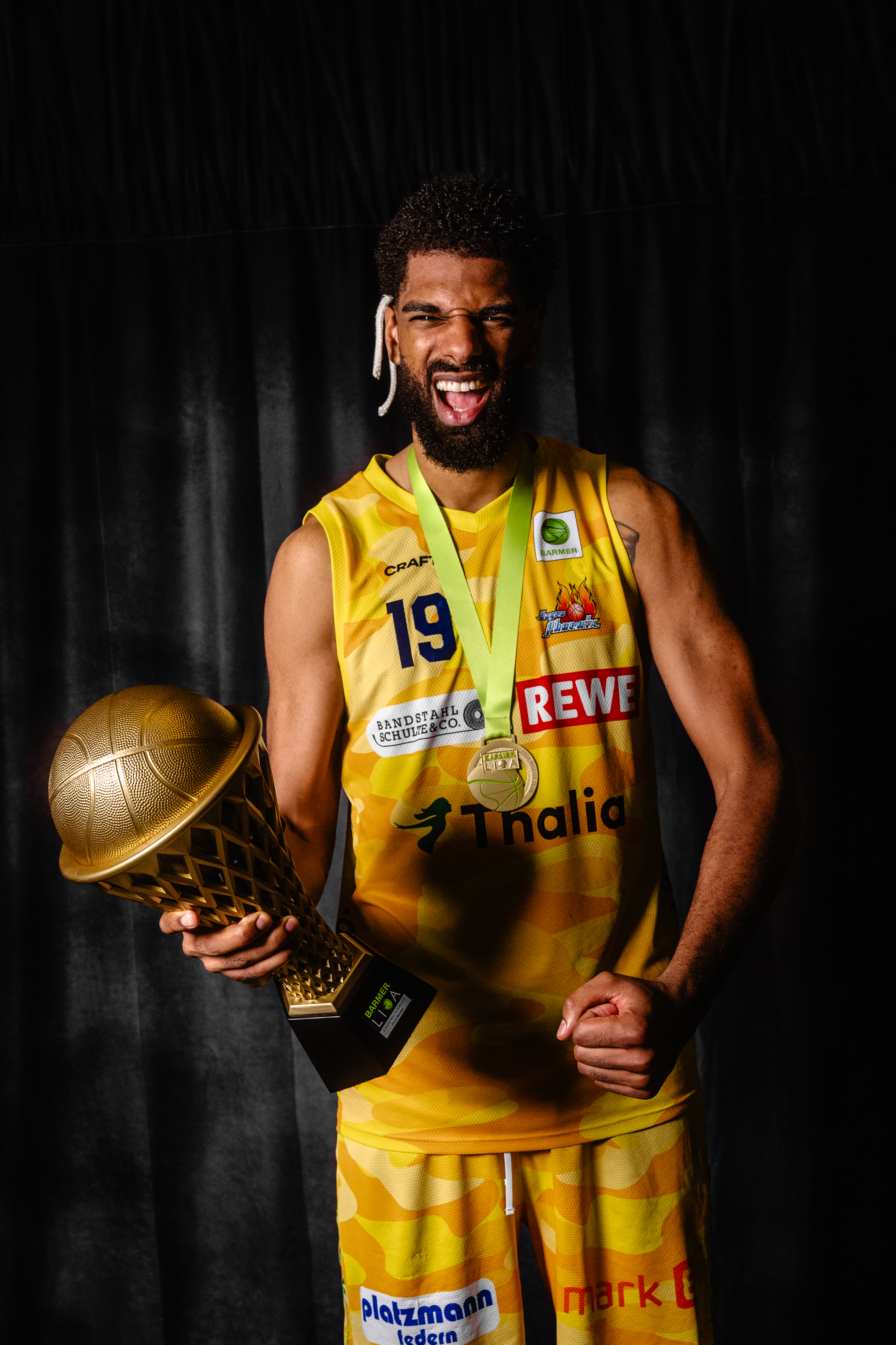Jubelnder Basketballspieler in gelbem Trikot mit Pokal und Medaille