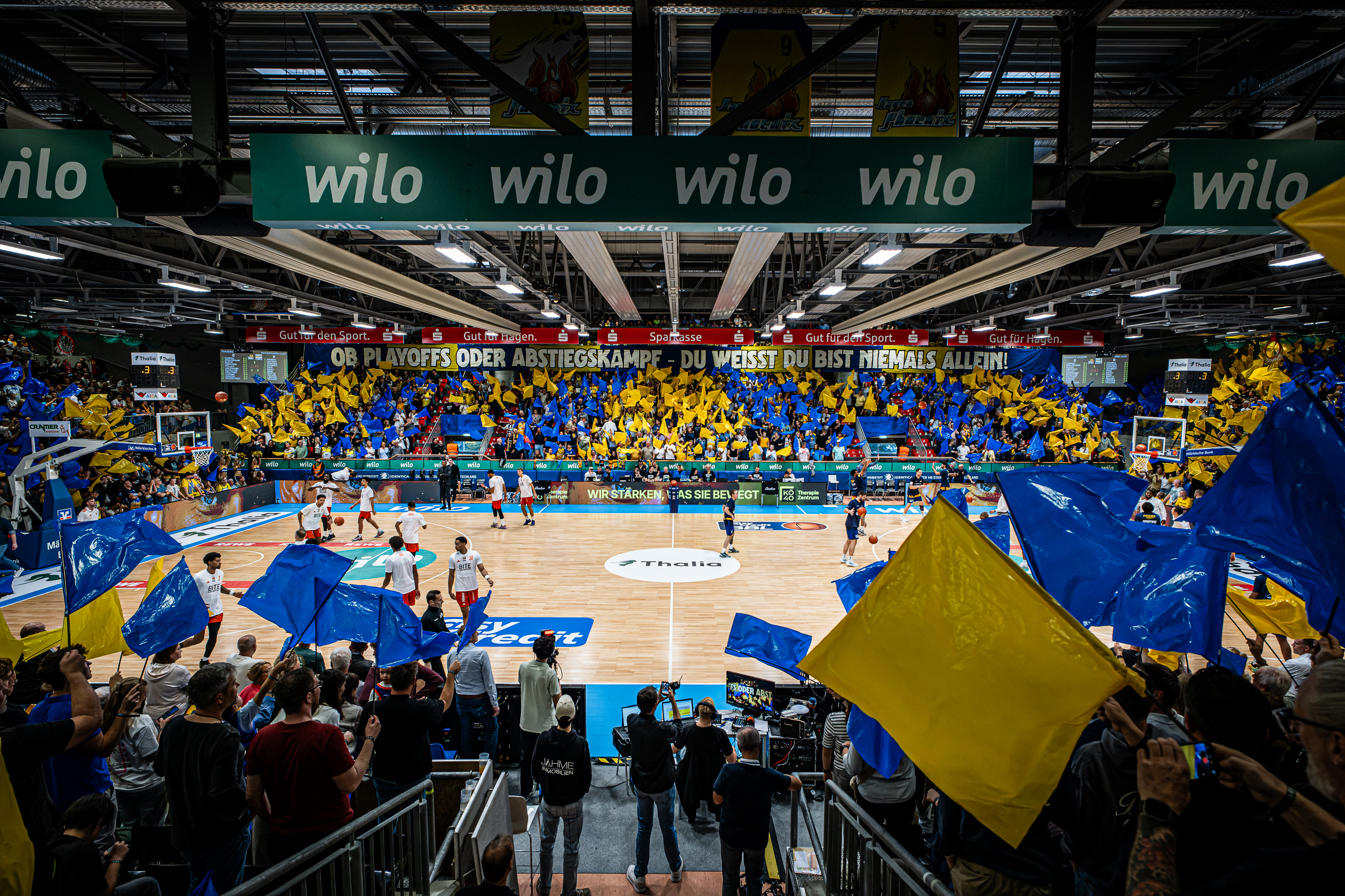 Basketballhalle mit begeisterten Fans die blaue und gelbe Fahnen schwenken