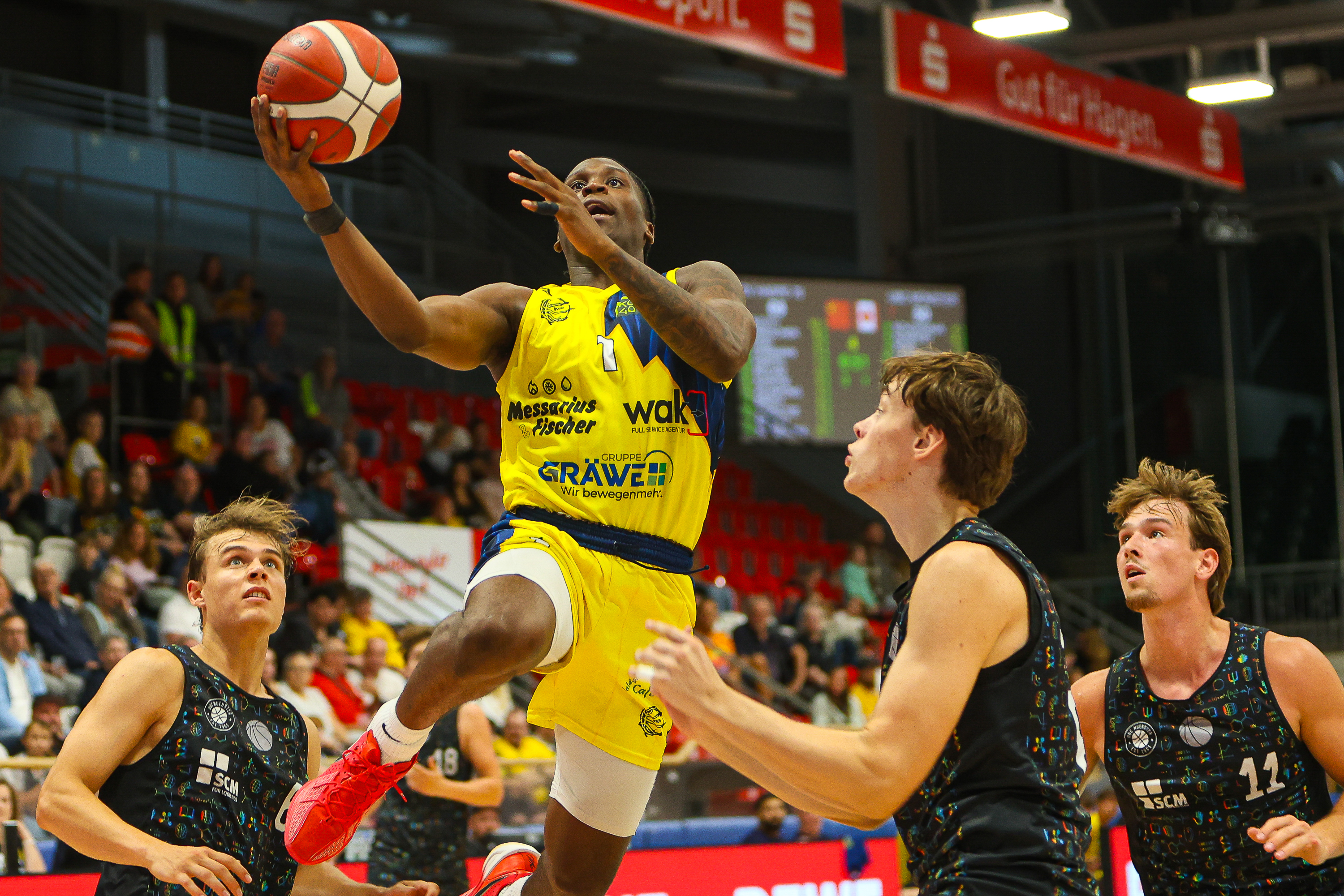 Basketballspieler im gelben Trikot springt konzentriert zum Korbleger auf