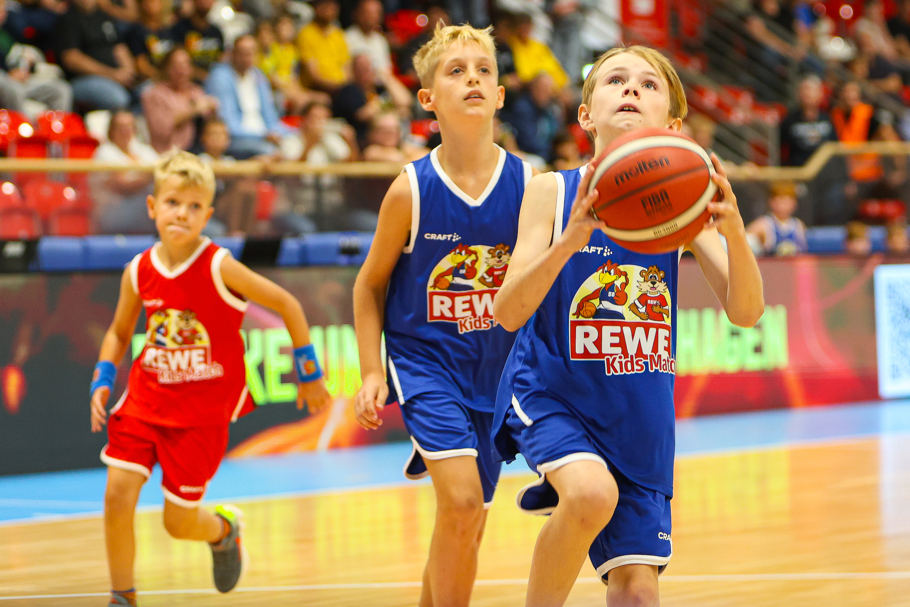 Konzentrierter blonder Junge im blauen Trikot laeuft mit Basketball zum Korb