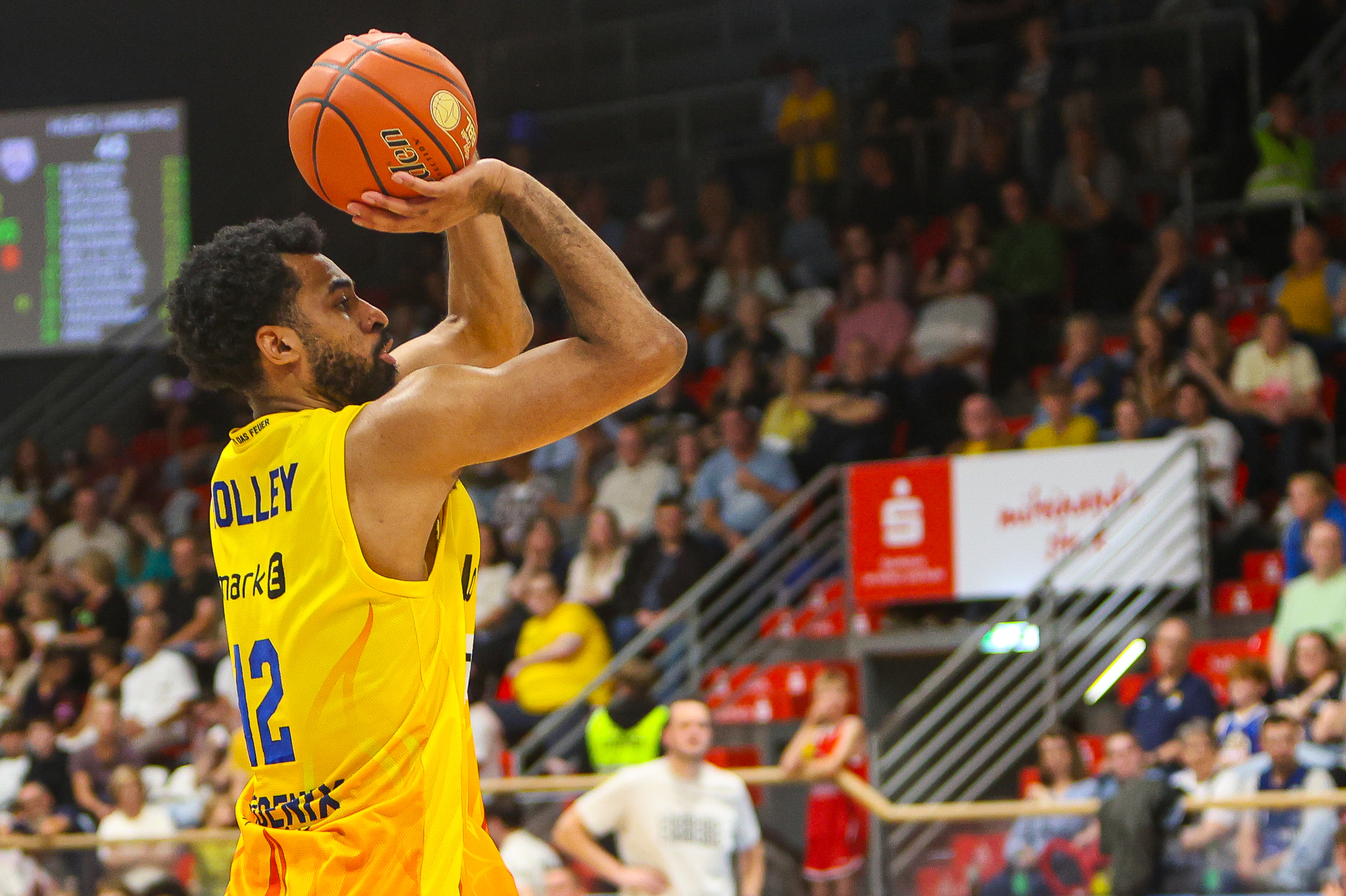 Basketballspieler im gelben Trikot mit Nummer 12 wirft konzentriert den Ball
