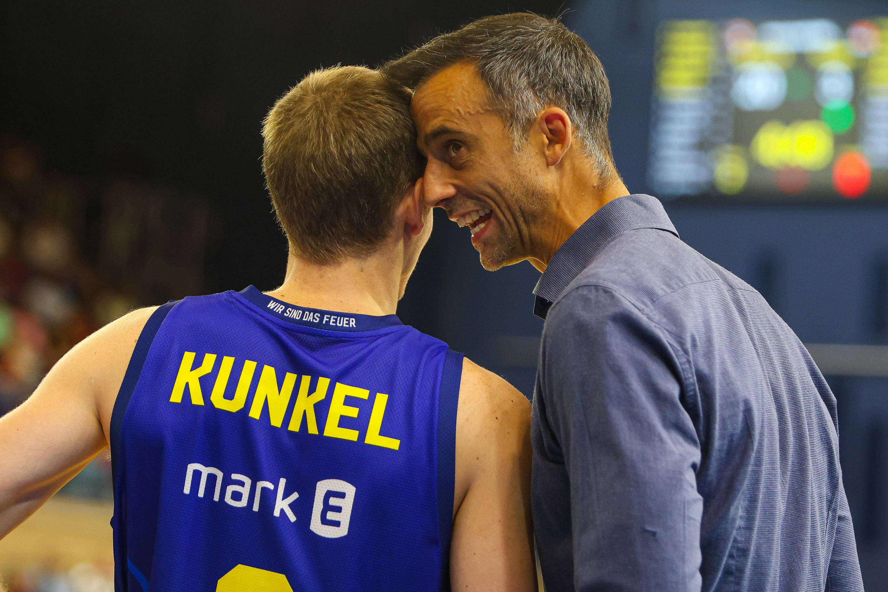 Laechelnder Mann im blauen Hemd im Gespraech mit Basketballspieler Kunkel