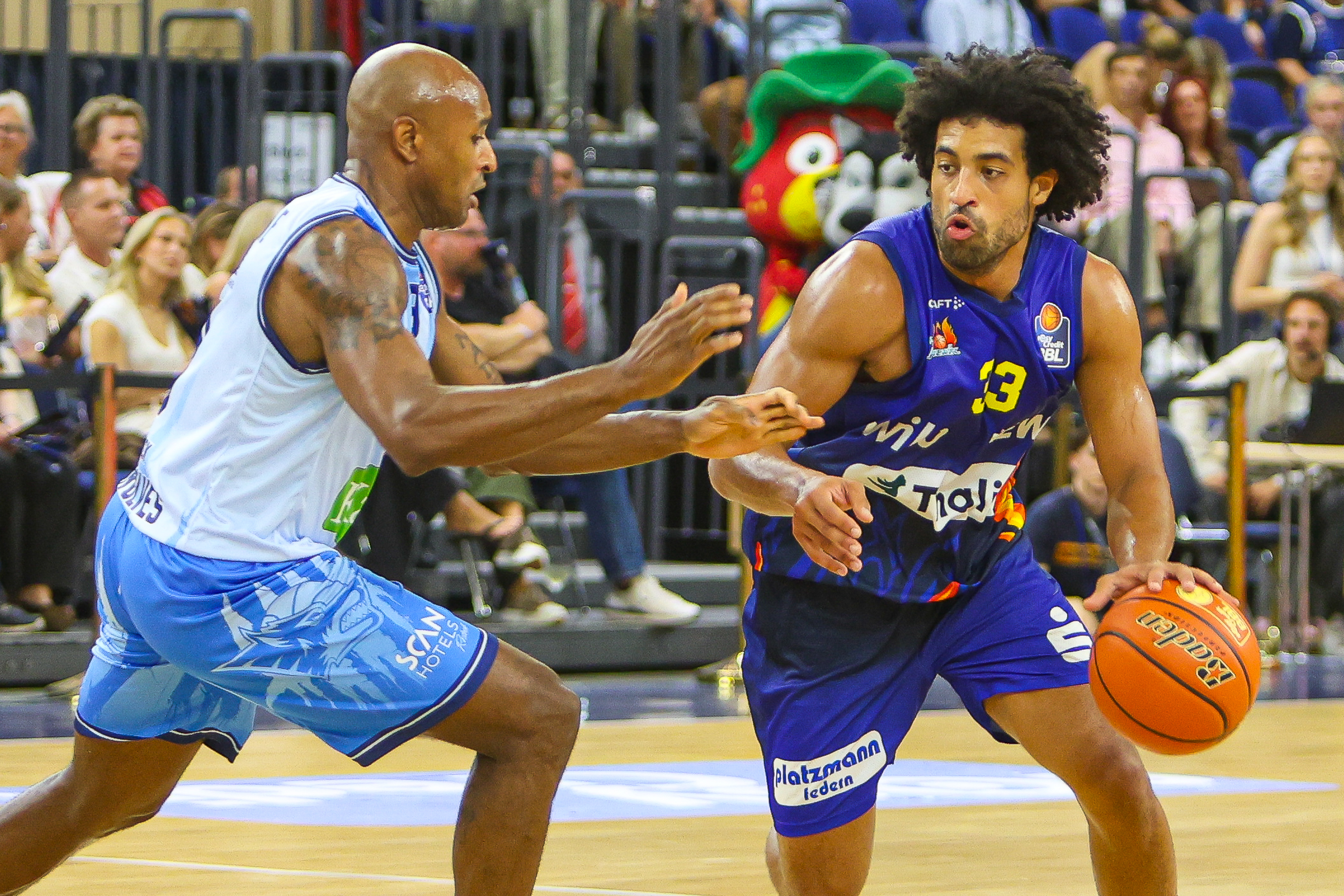 Zwei Basketballspieler in Blau kaempfen konzentriert um den orangefarbenen Ball
