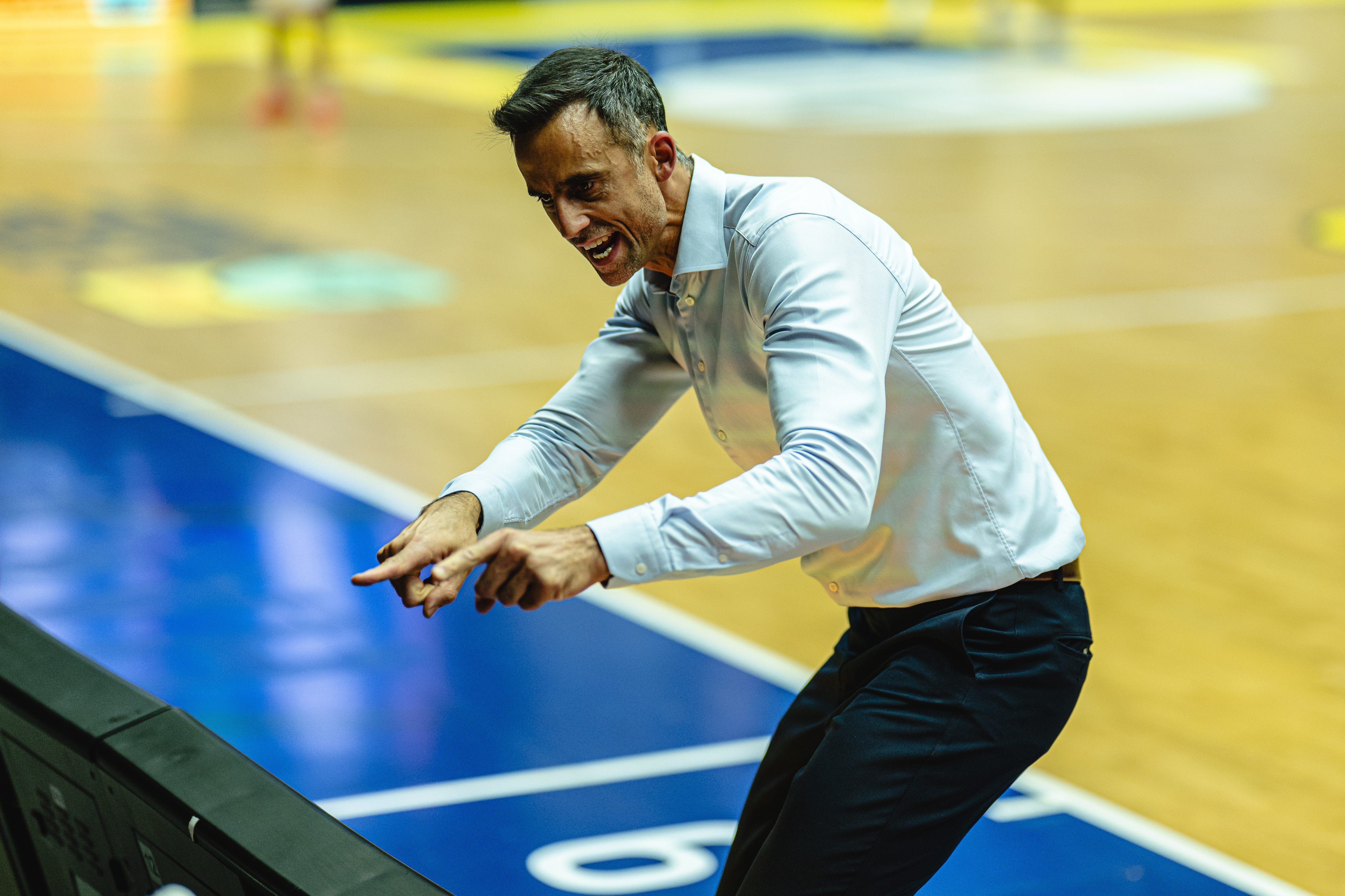 Ein Trainer im weissen Hemd zeigt engagiert rufend zur Seite am Spielfeldrand