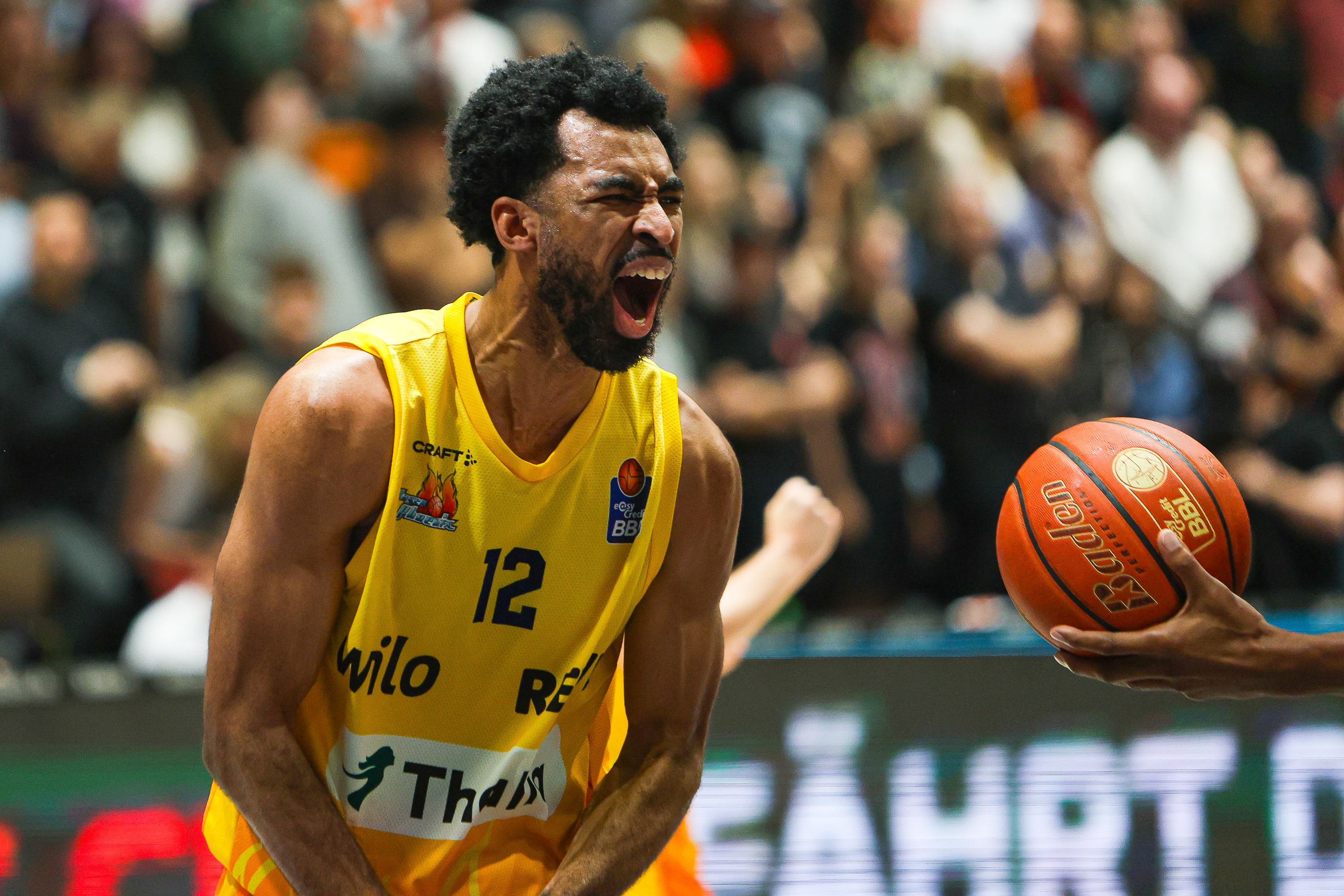 Jubelnder Basketballspieler im gelben Trikot Nummer zwoelf mit Ball