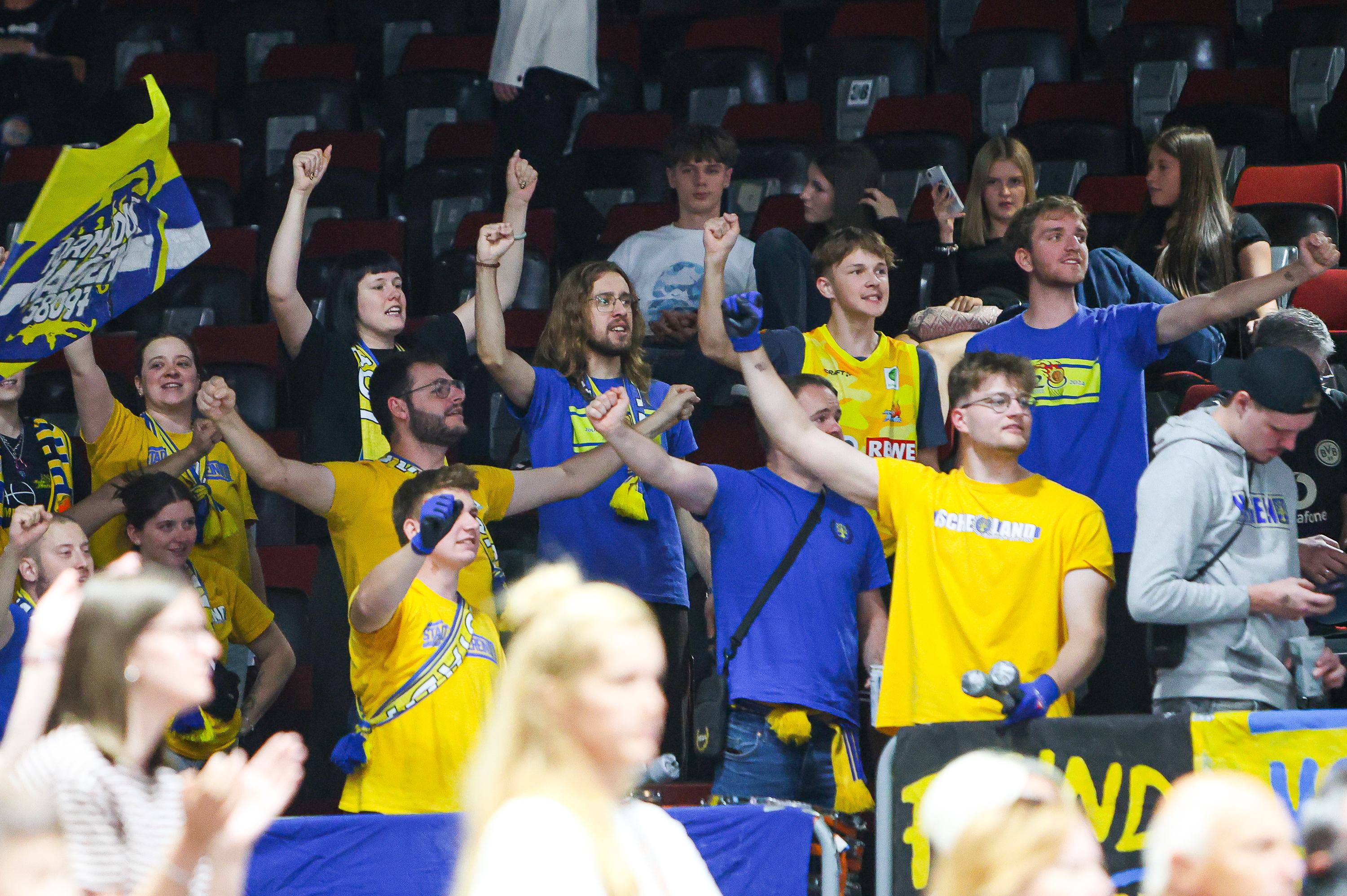 Jubelnde Fans in blau gelben Trikots feiern begeistert mit erhobenen Armen