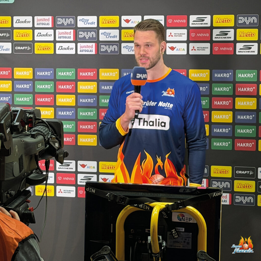Ein Basketballspieler im blauen Trikot gibt konzentriert ein Interview