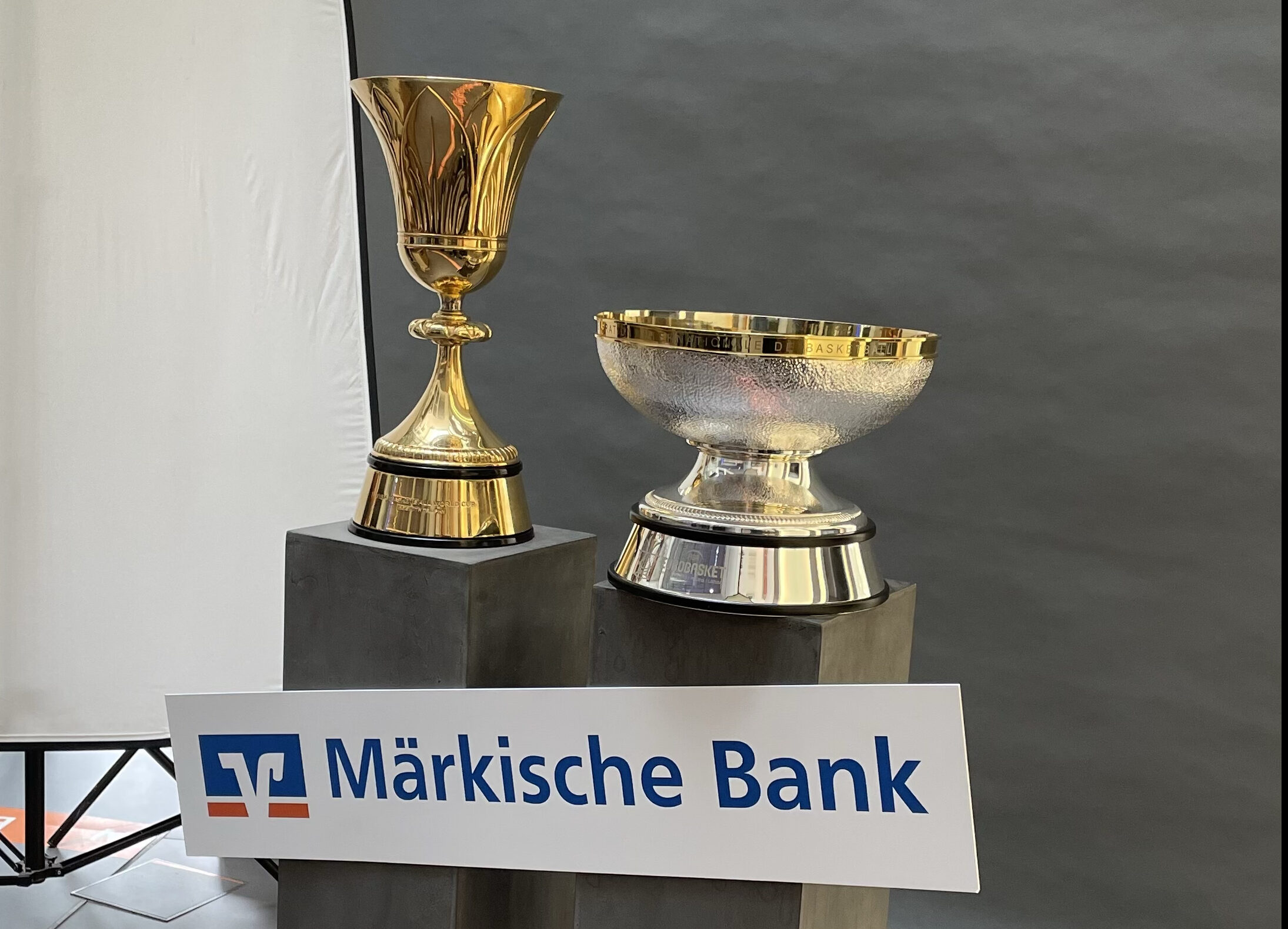 Zwei goldene Pokale auf Sockeln mit einem Schild der Maerkischen Bank
