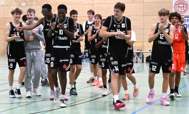 Laechelnde Basketballmannschaft in schwarzen Trikots geht durch die Halle