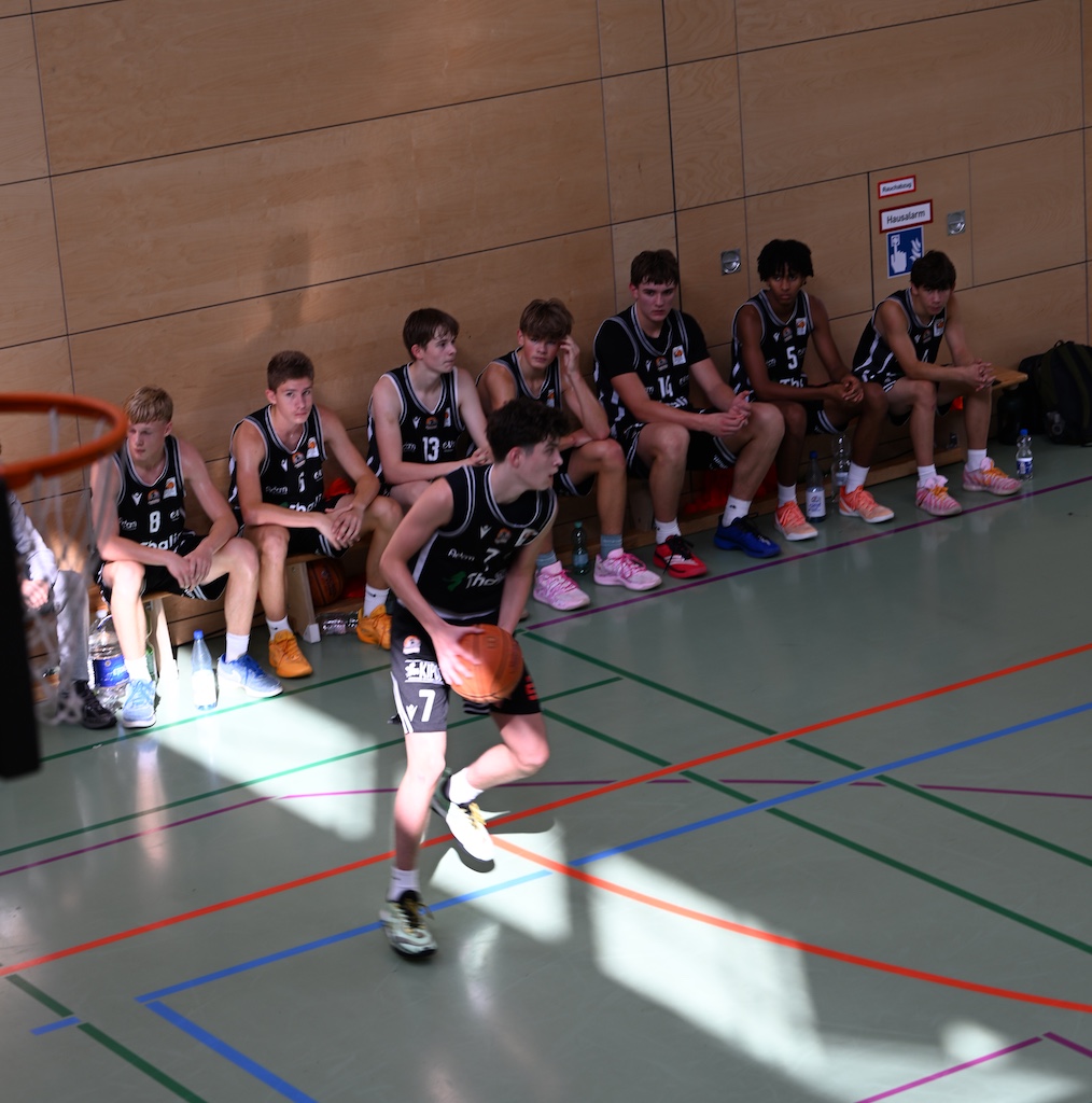 Junger Basketballspieler mit Nummer 7 dribbelt konzentriert vor der Ersatzbank