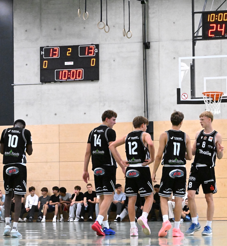 Fuenf junge Basketballspieler in schwarzen Trikots stehen konzentriert in der Halle