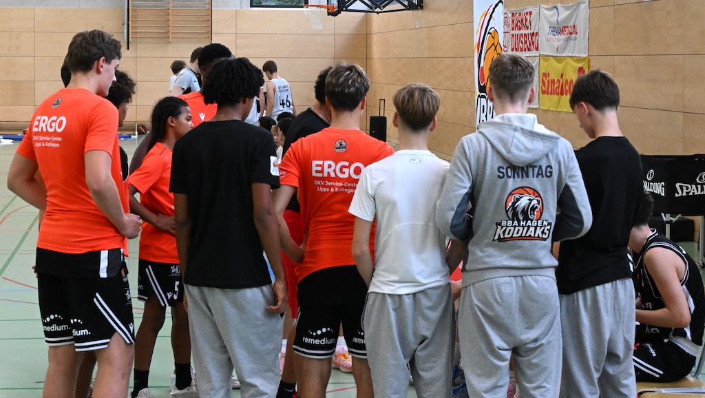 Junge Basketballspieler in orangefarbenen und schwarzen Trikots stehen in einer Halle zusammen