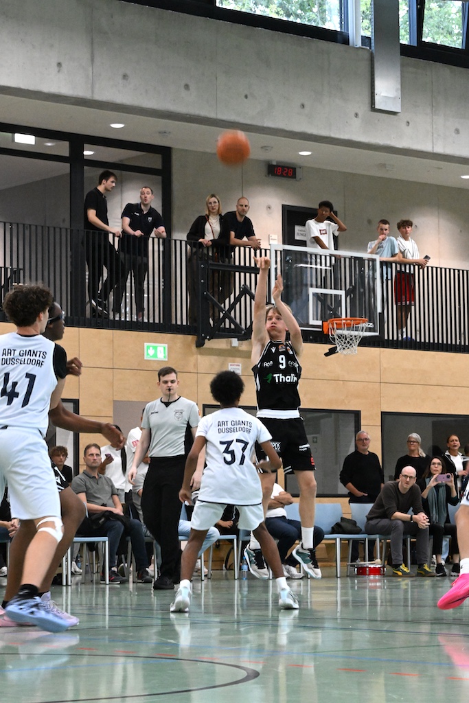 Basketballspieler in schwarzem Trikot Nummer neun beim konzentrierten Wurf zum Korb