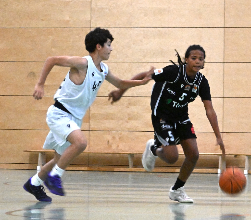 Zwei junge Basketballspieler in Weiss und Schwarz kaempfen um den Ball