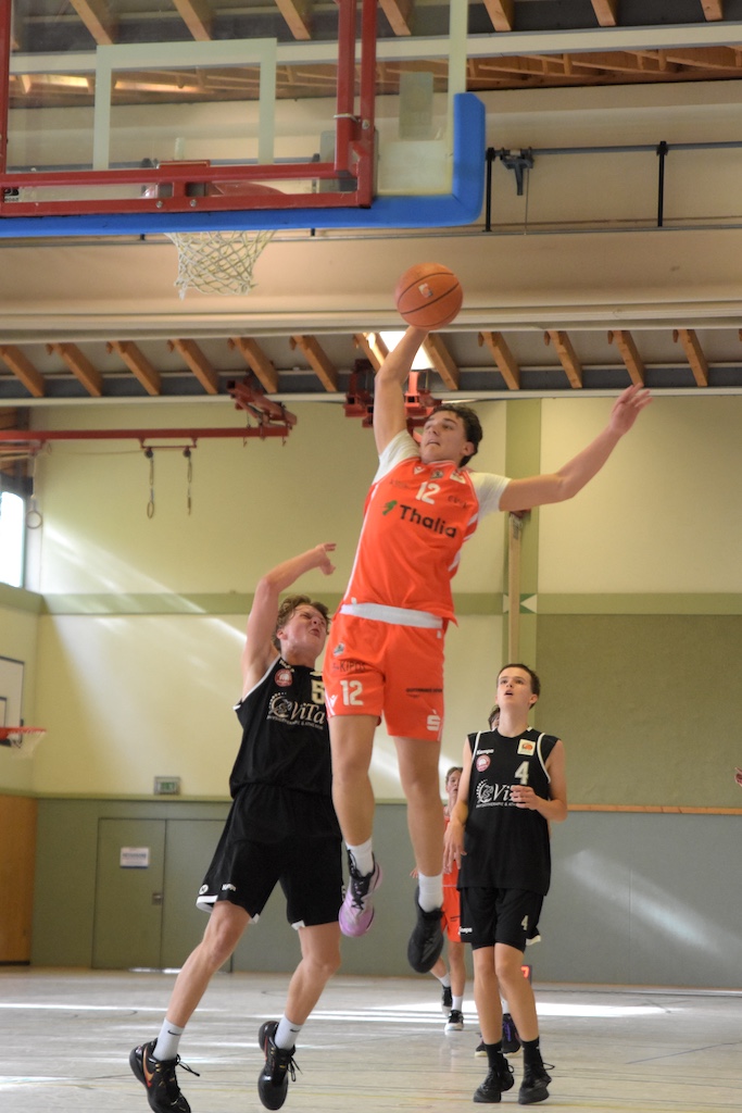 Basketballspieler in orangem Trikot springt konzentriert zum Korbwurf hoch