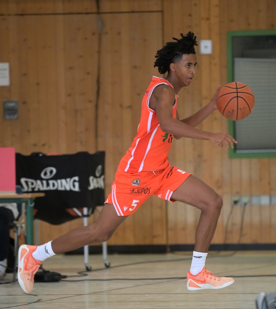 Junger Basketballspieler in orangem Trikot dribbelt konzentriert den Ball