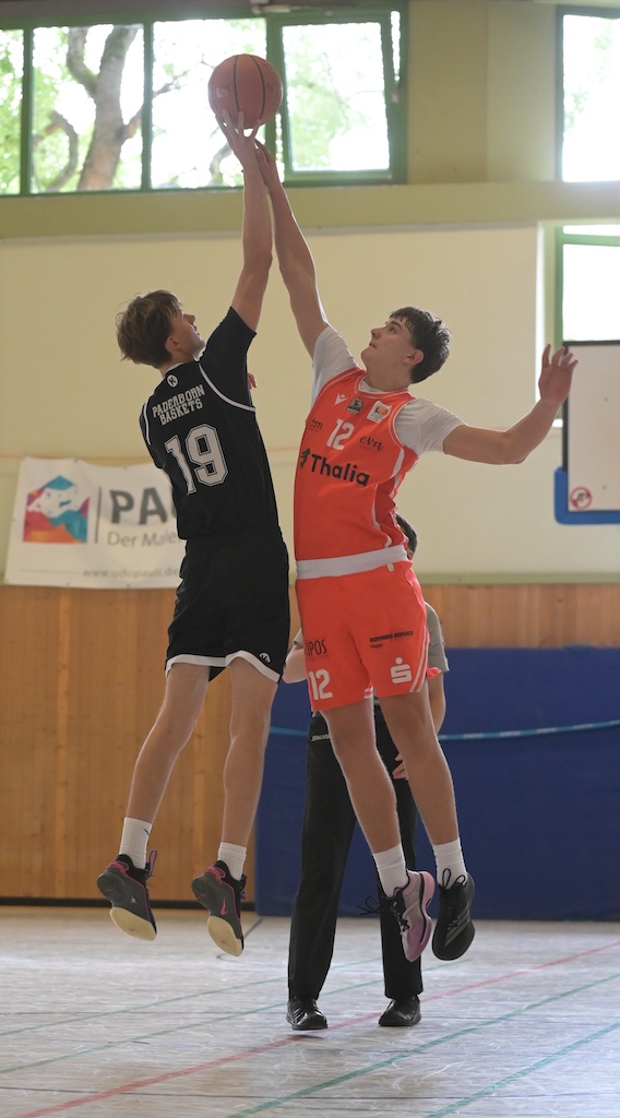 Zwei junge Basketballspieler in Schwarz und Orange springen konzentriert zum Ball