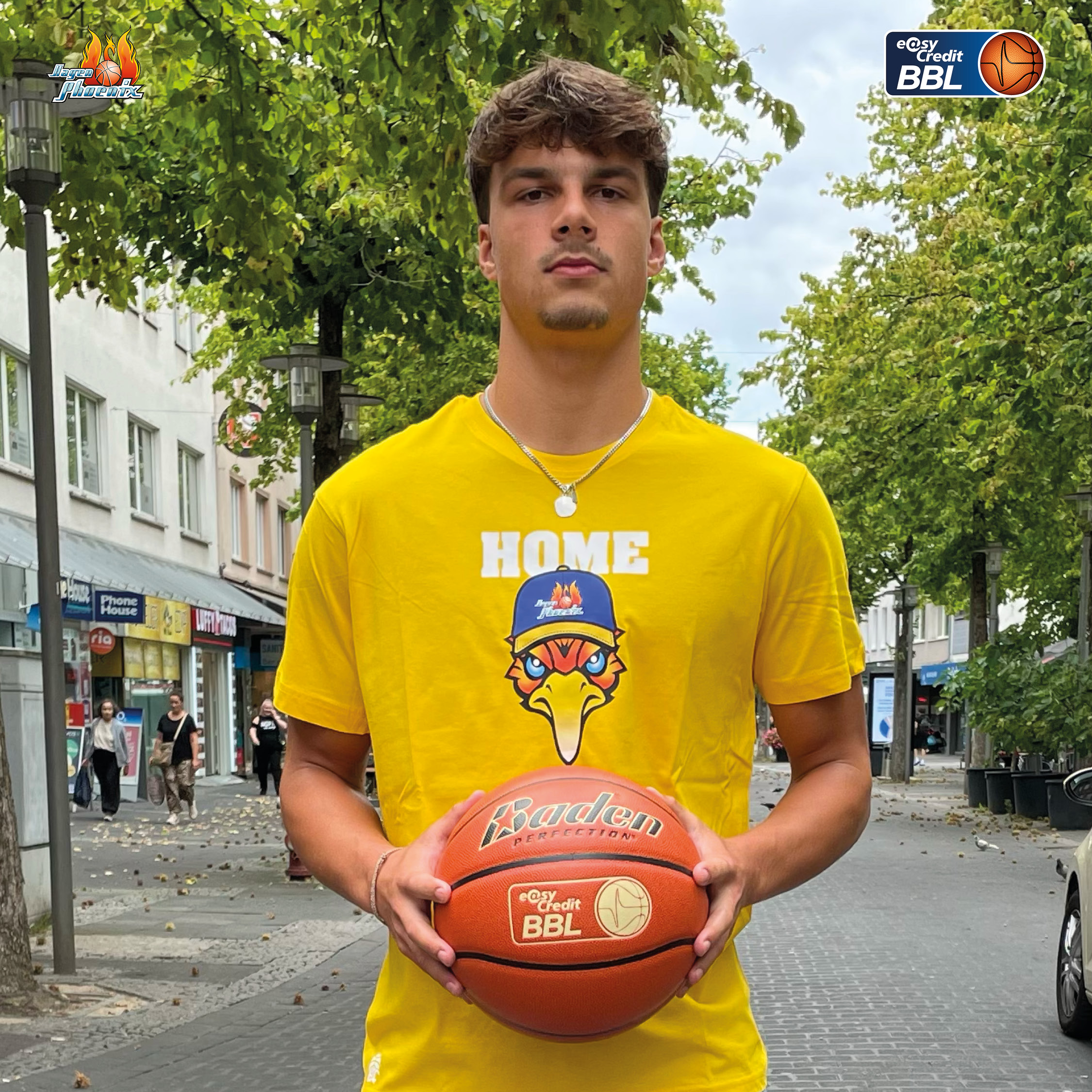 Junger Mann mit ernstem Blick im gelben Trikot haelt einen Basketball
