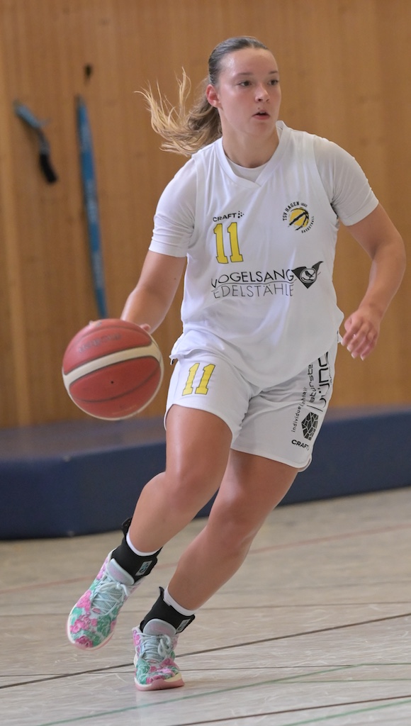 Junge Basketballspielerin mit Nummer 11 dribbelt konzentriert in weissem Trikot