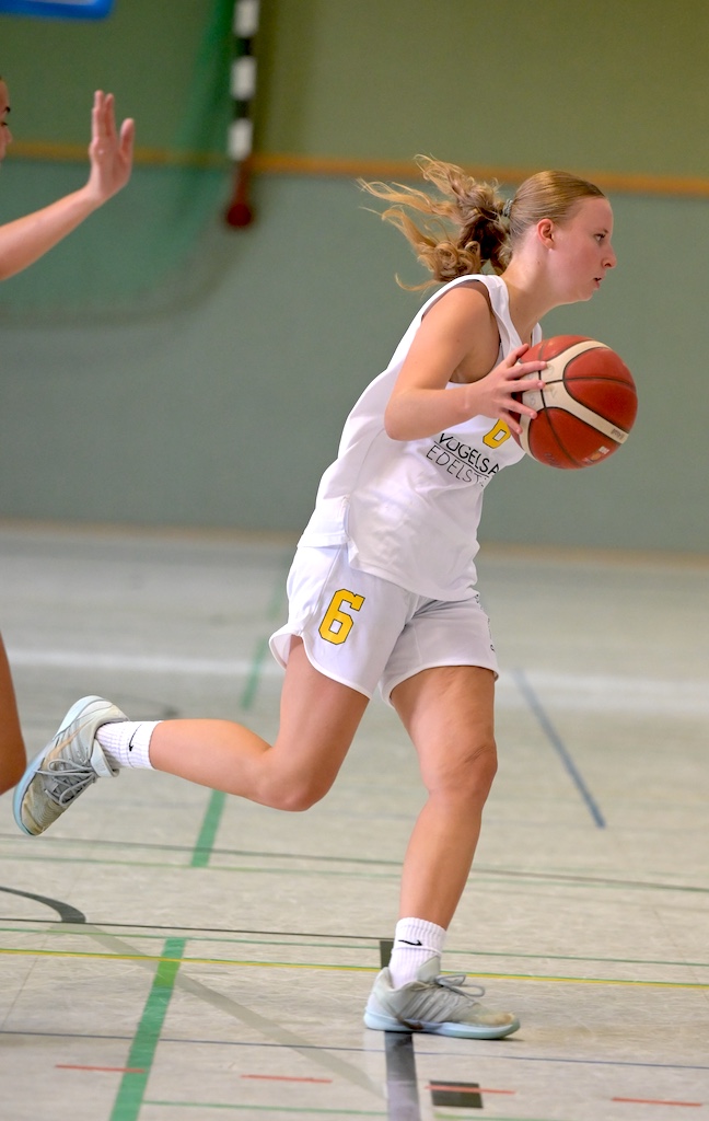 Konzentrierte Basketballspielerin in weissem Trikot Nummer 6 mit orangem Ball
