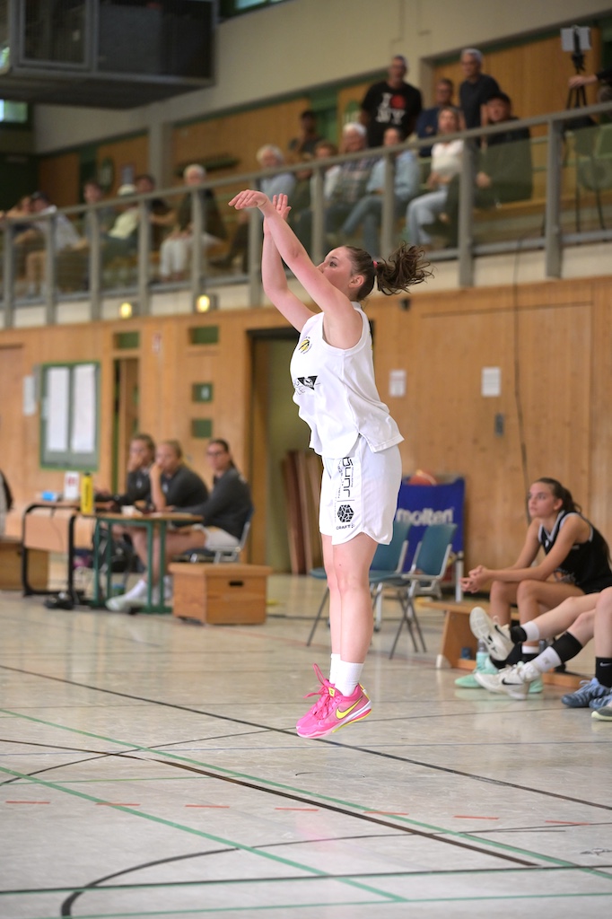Basketballspielerin in weissem Trikot mit pinken Schuhen springt konzentriert