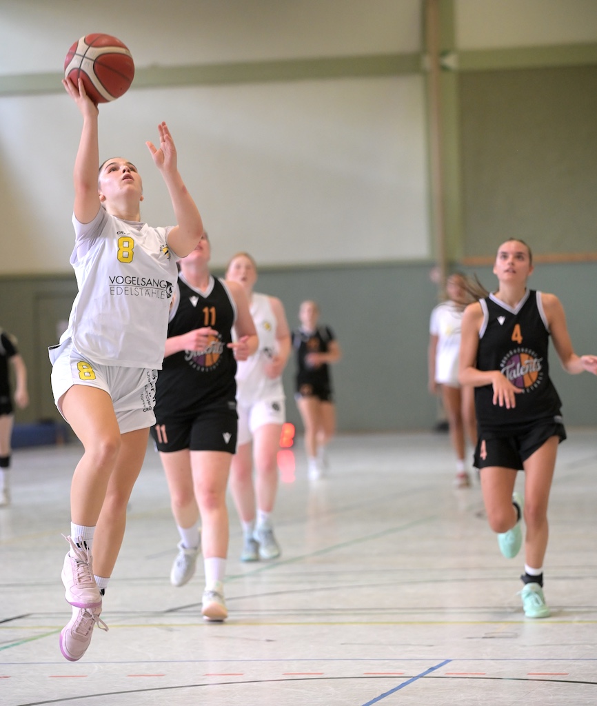 Basketballspielerin mit Nummer 8 in Weiss springt konzentriert zum Korbwurf