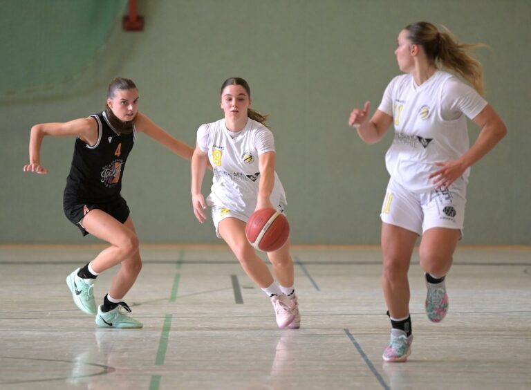 Drei Basketballspielerinnen in Aktion mit fokussierten Ausdruecken in einer Halle