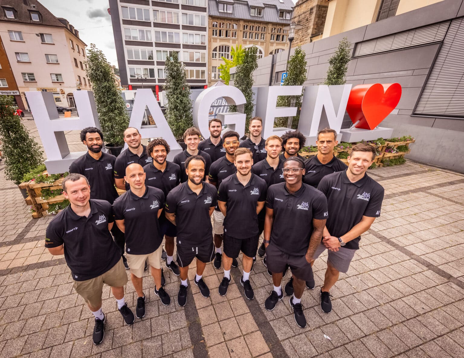 Laechelnde Sportmannschaft in schwarzen Poloshirts vor grossem Hagen Schriftzug