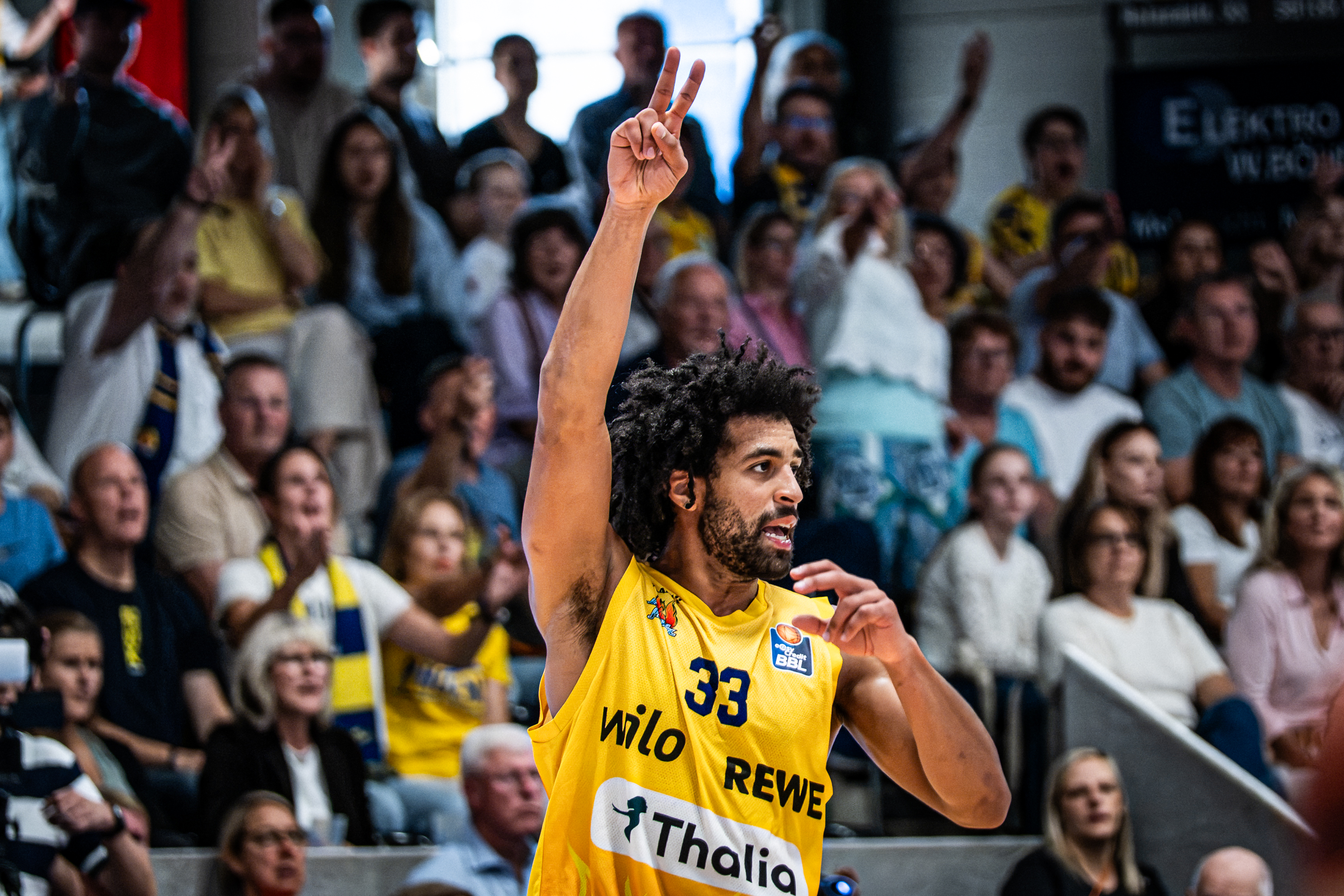 Basketballspieler im gelben Trikot Nummer 33 zeigt jubelnd zwei Finger
