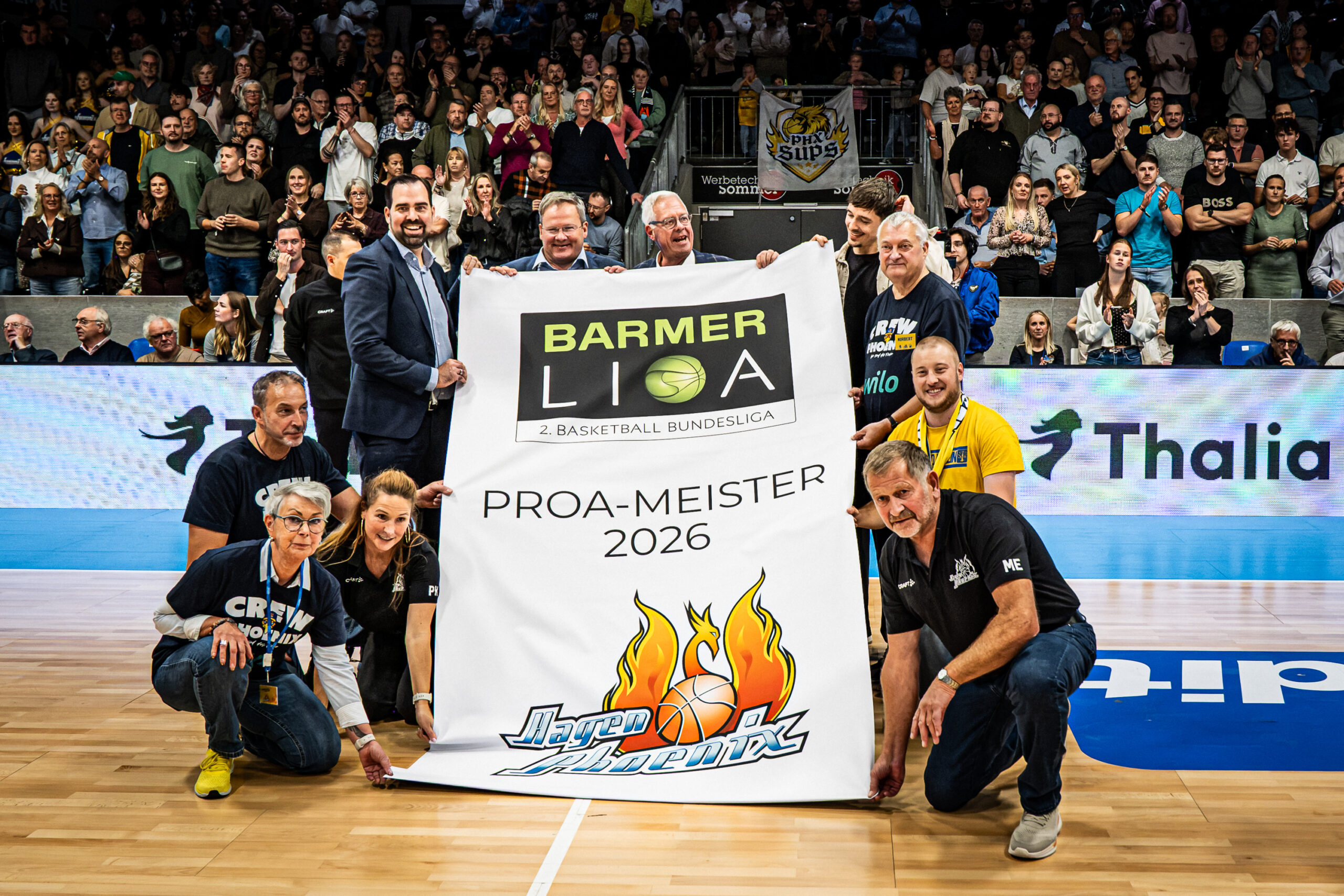 Laechelnde Personen halten stolz ein Banner zum ProA-Meister 2026 in der Halle