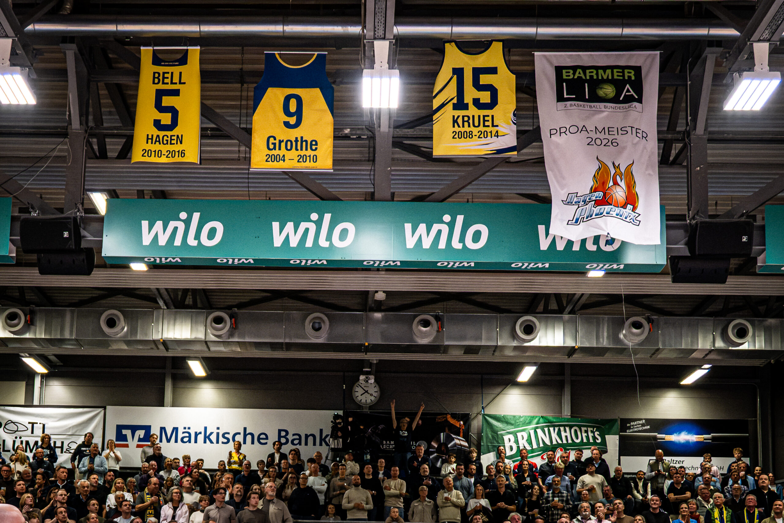 Geehrte Trikots in Gelb und Blau haengen ueber Zuschauern in einer Sporthalle