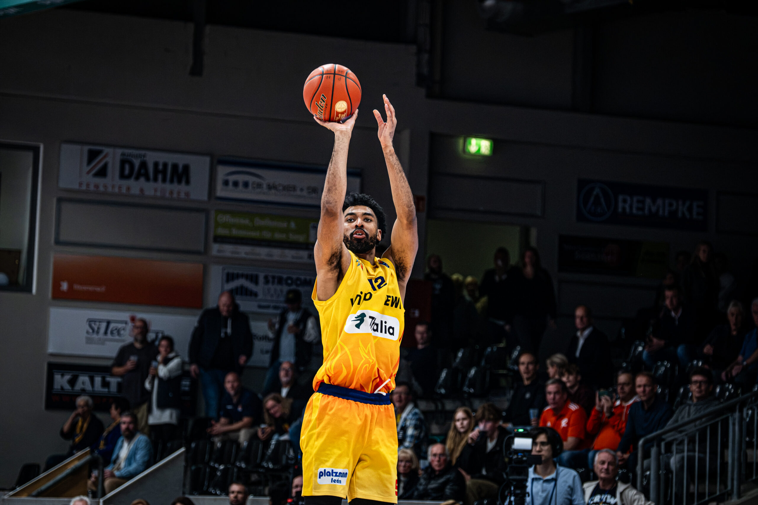 Ein Basketballspieler im gelben Trikot wirft konzentriert den Ball zum Korb