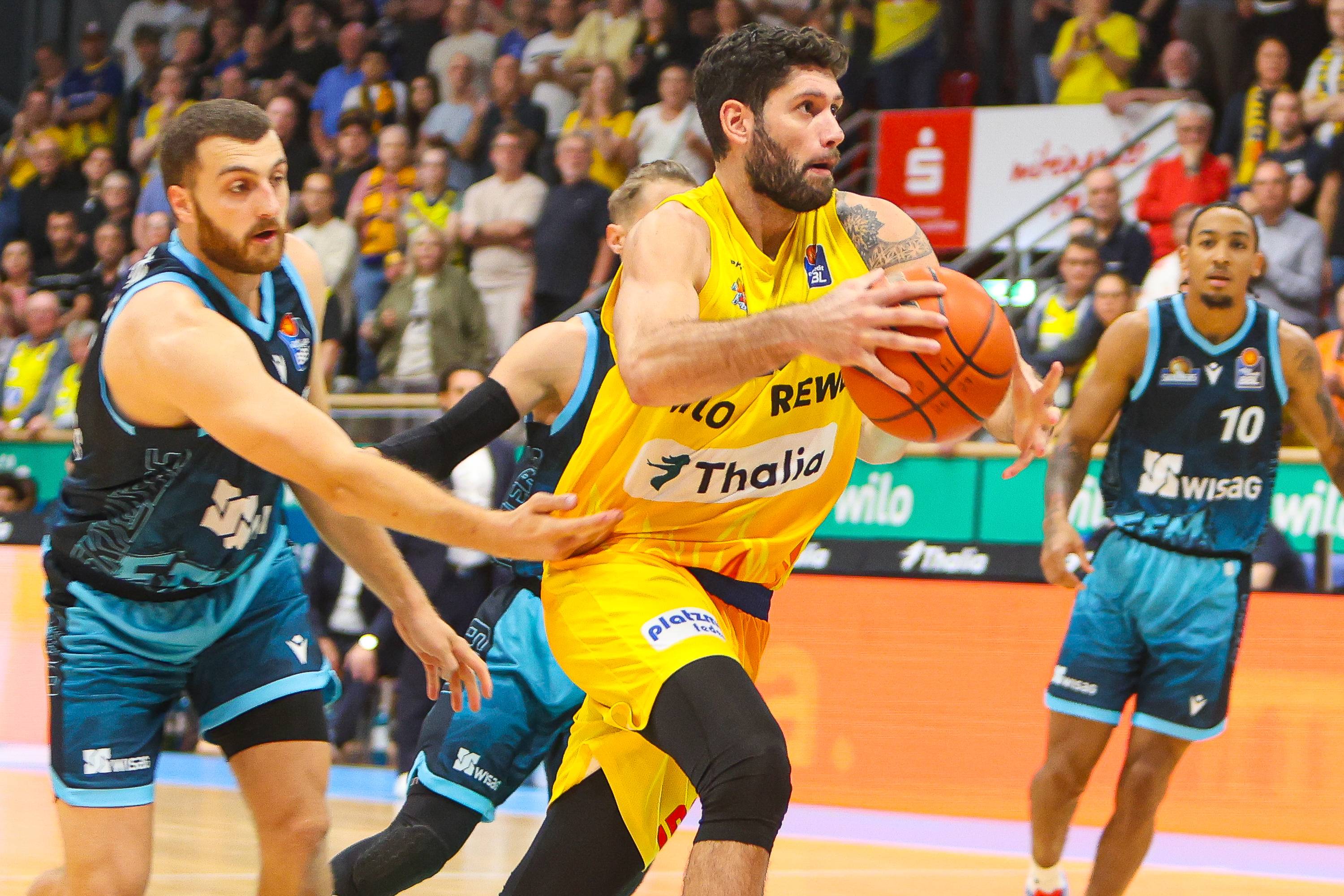 Basketballspieler im gelben Trikot mit Bart haelt konzentriert den Ball