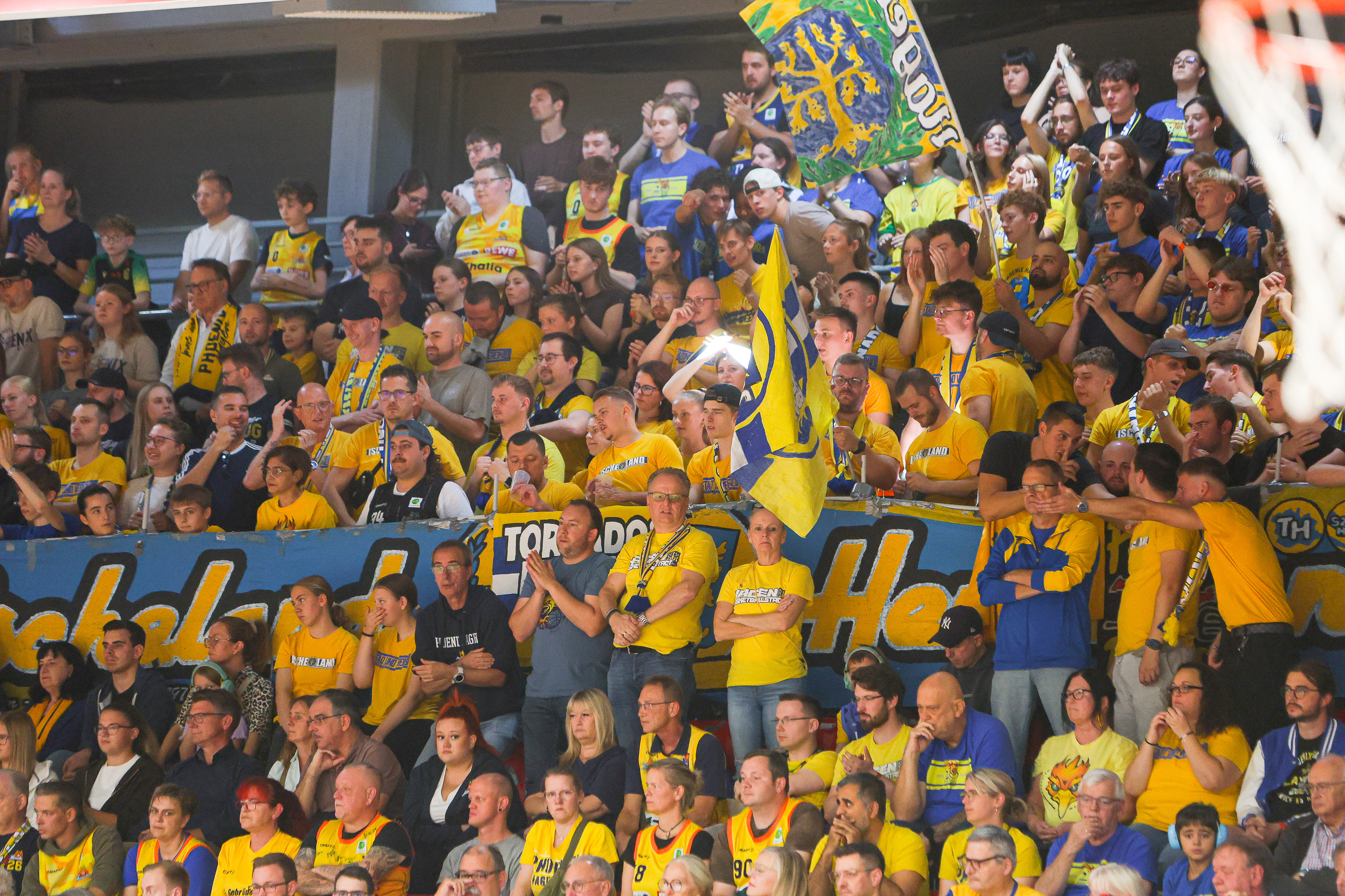 Gespannte Fans in Gelb und Blau mit Fahnen bei einem Basketballspiel