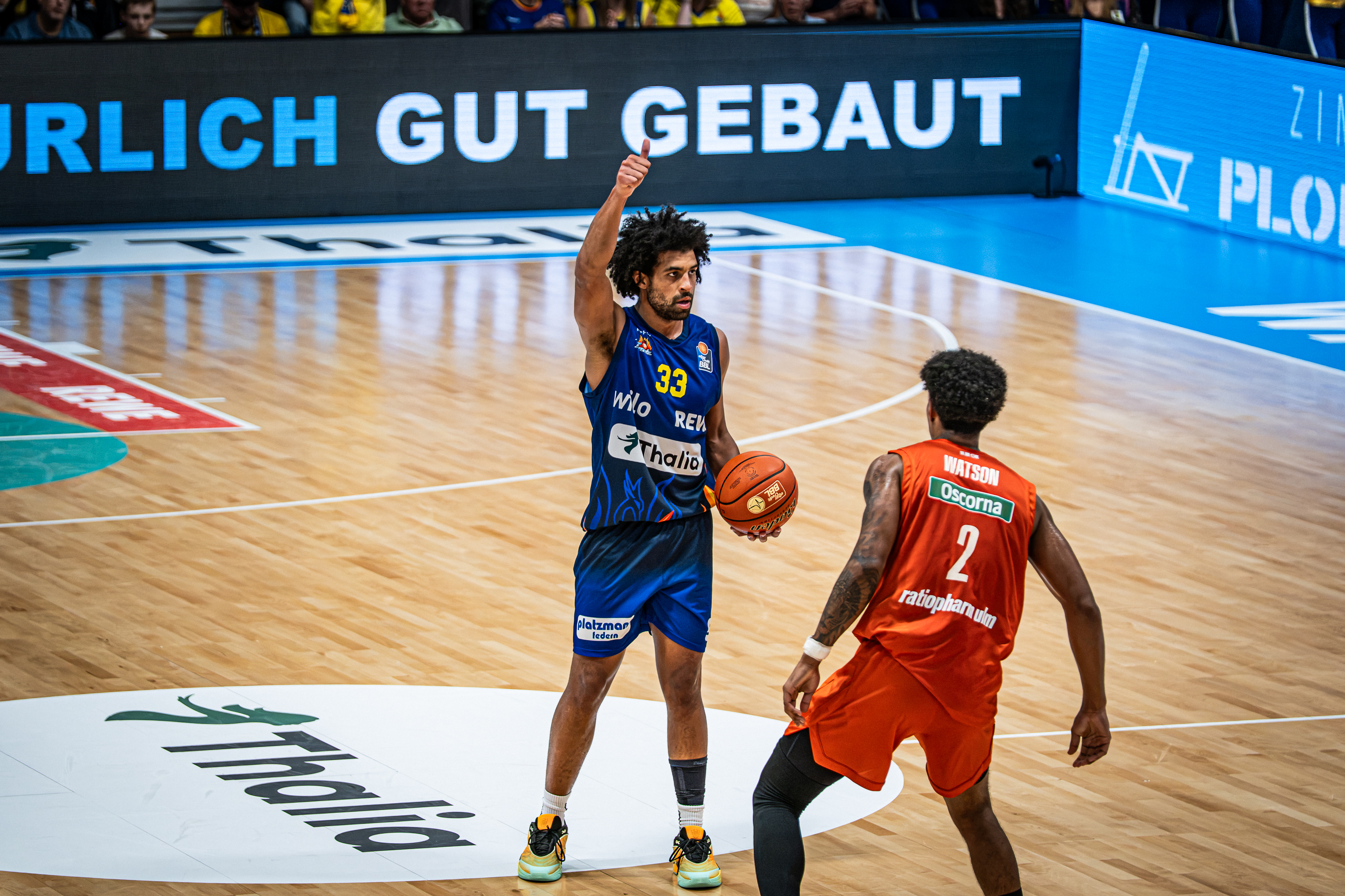 Basketballspieler im blauen Trikot mit Daumen hoch gegen Gegner in Orange