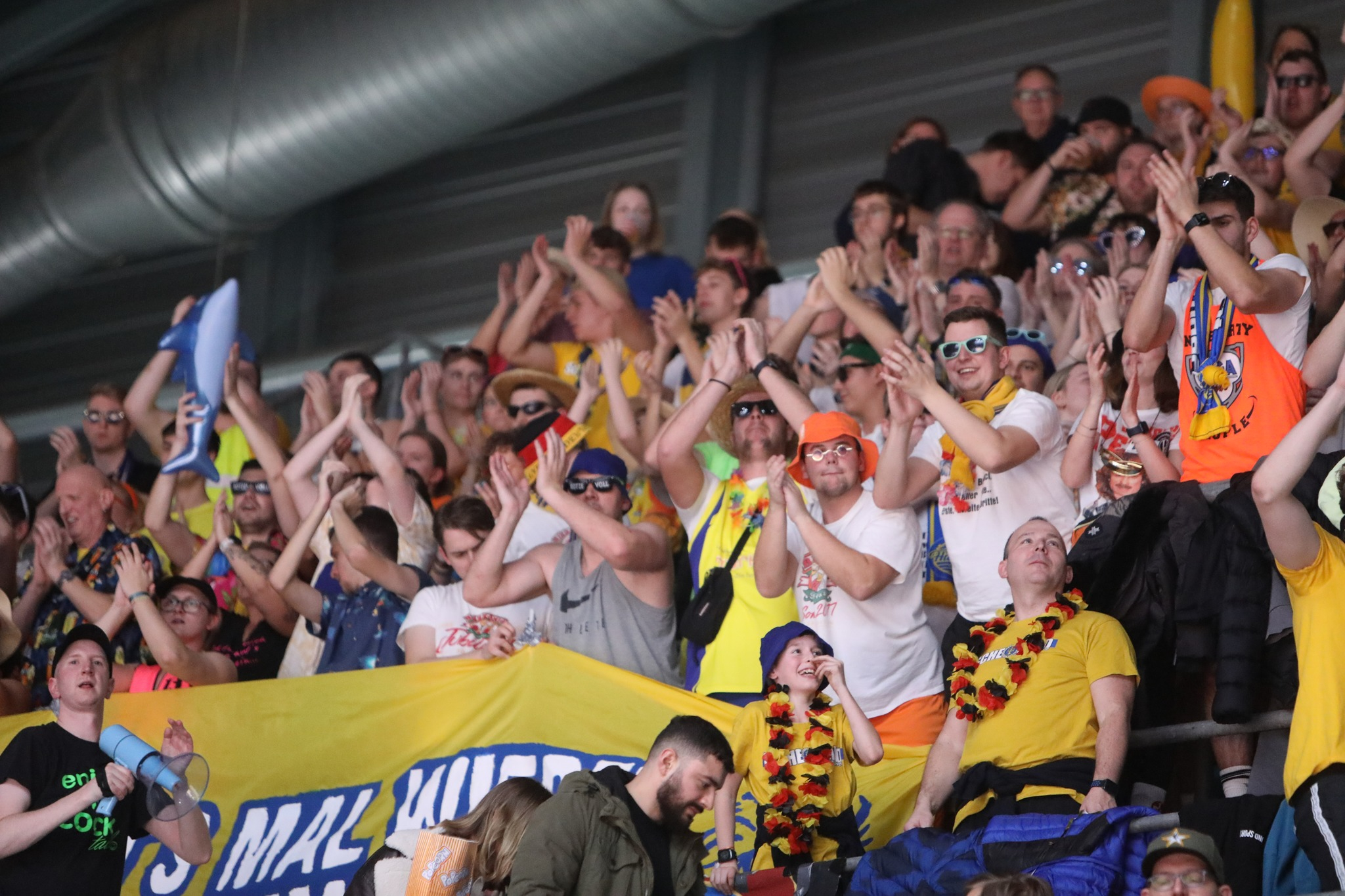 Jubelnde Fans in bunter Kleidung klatschen begeistert auf einer Tribuene