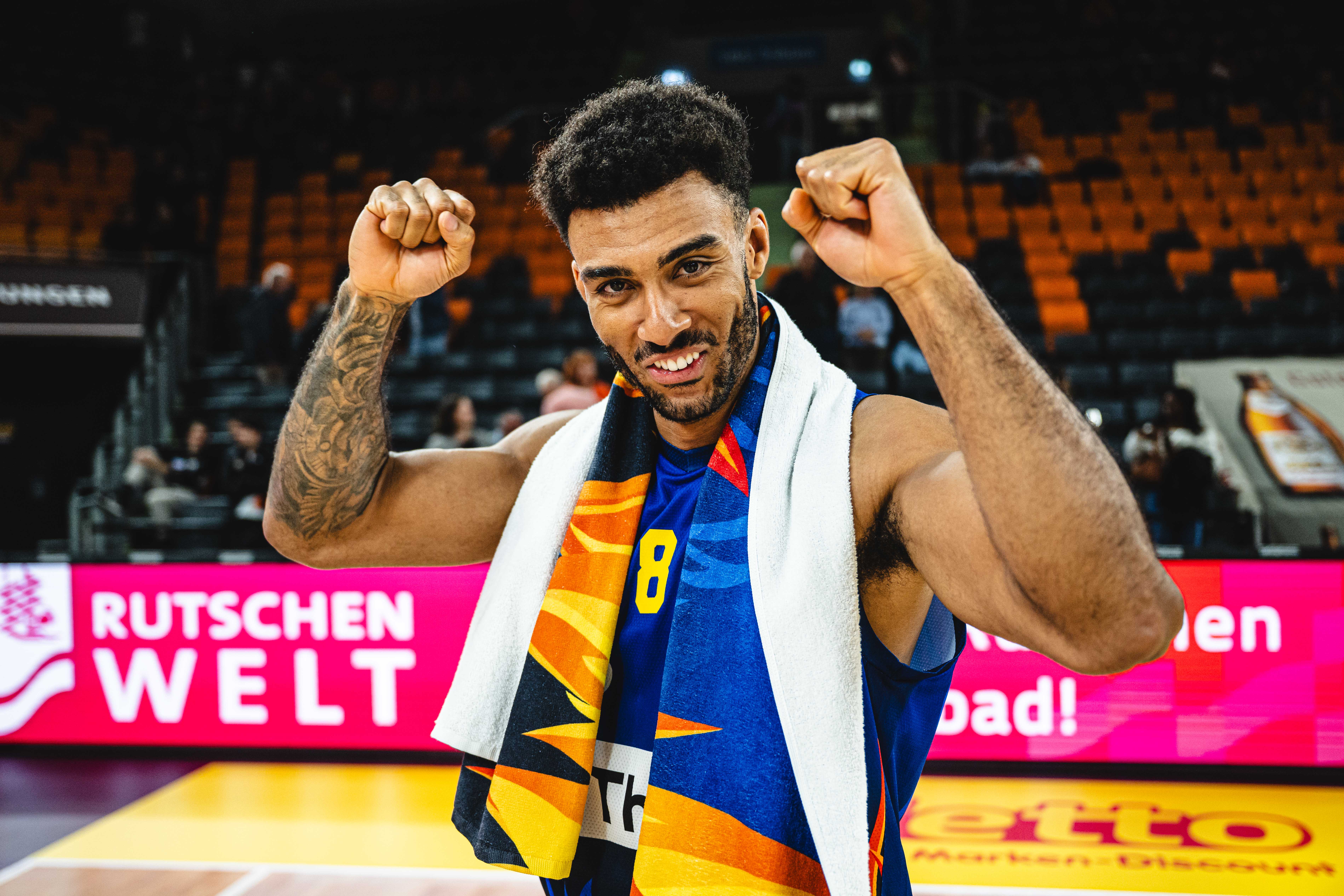 Laechelnder Basketballspieler im blauen Trikot zeigt jubelnd beide Fäuste