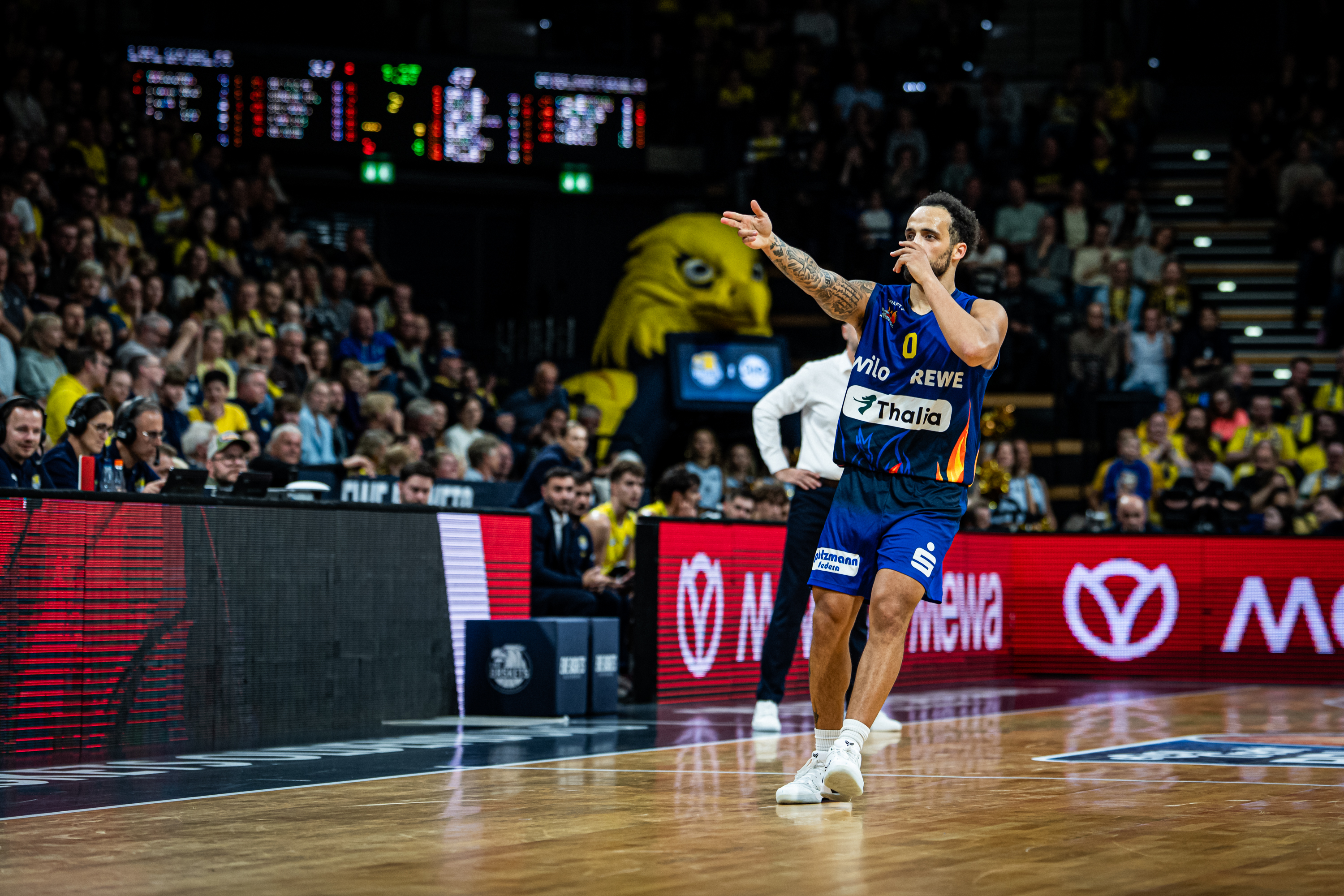 Basketballspieler in blauem Trikot mit Tattoos feiert jubelnd in einer Halle