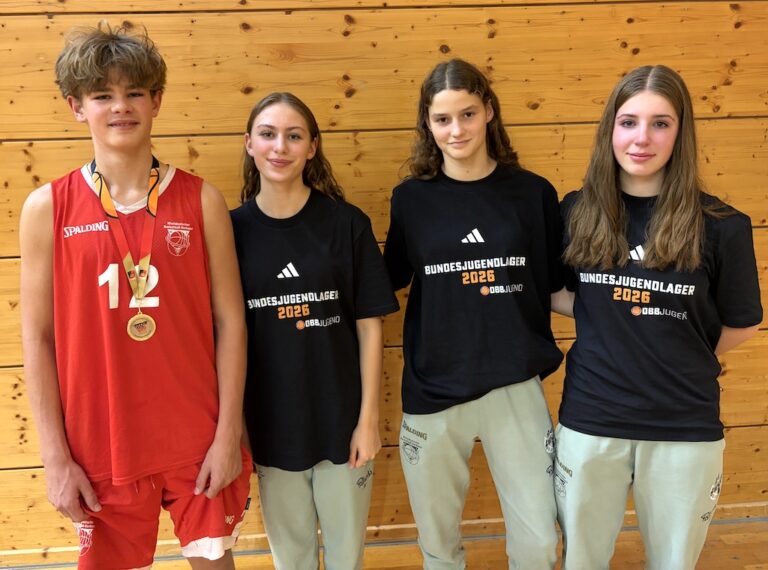 Vier laechelnde Jugendliche in Sportkleidung stehen vor einer Holzwand