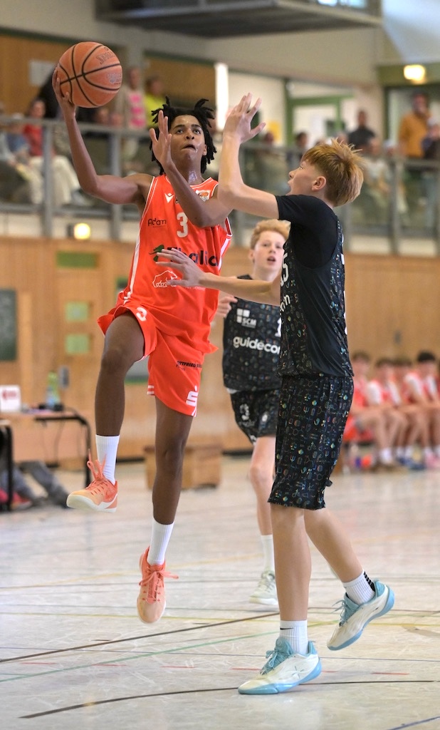 Junger Spieler in orangem Trikot springt konzentriert zum Korbwurf