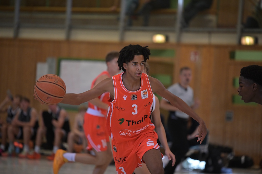 Junger Basketballspieler mit Dreadlocks im orangefarbenen Trikot dribbelt konzentriert