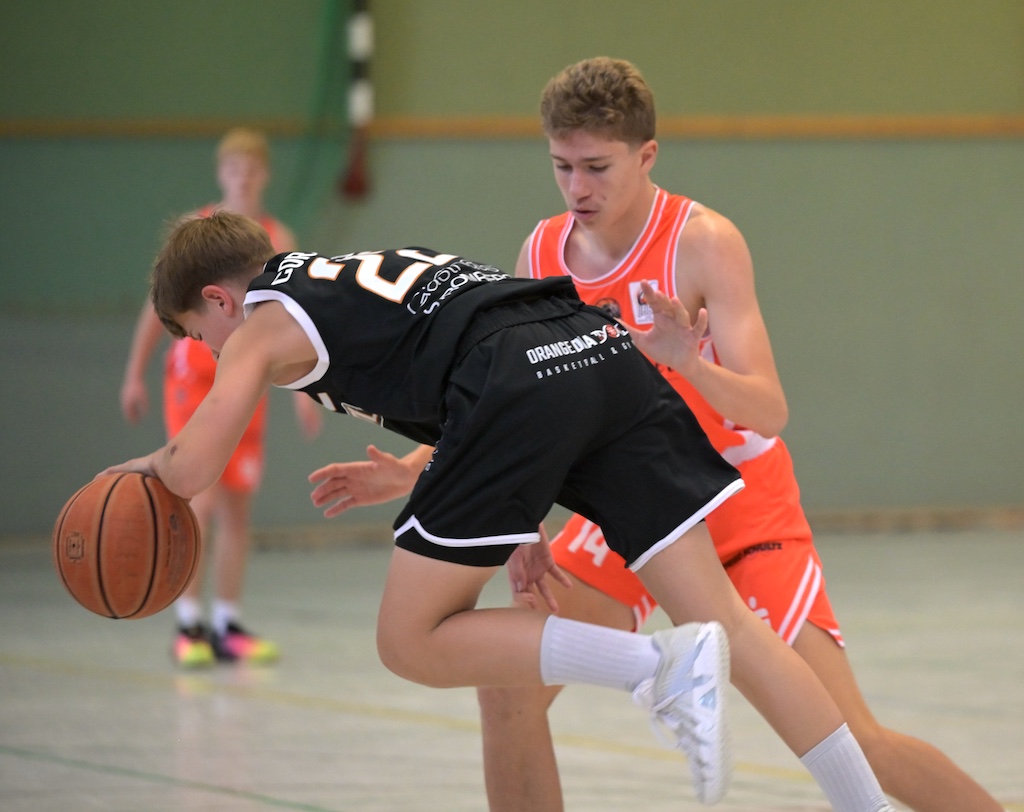 Zwei junge Basketballspieler in Schwarz und Orange kaempfen um den Ball