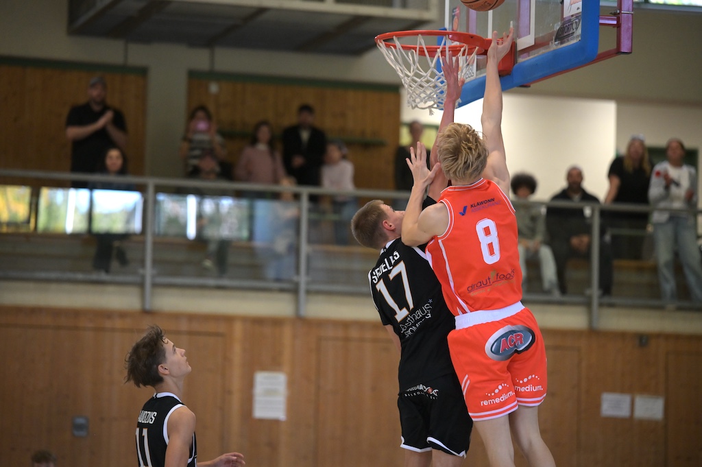 Zwei Basketballspieler in Orange und Schwarz kaempfen konzentriert um den Korb
