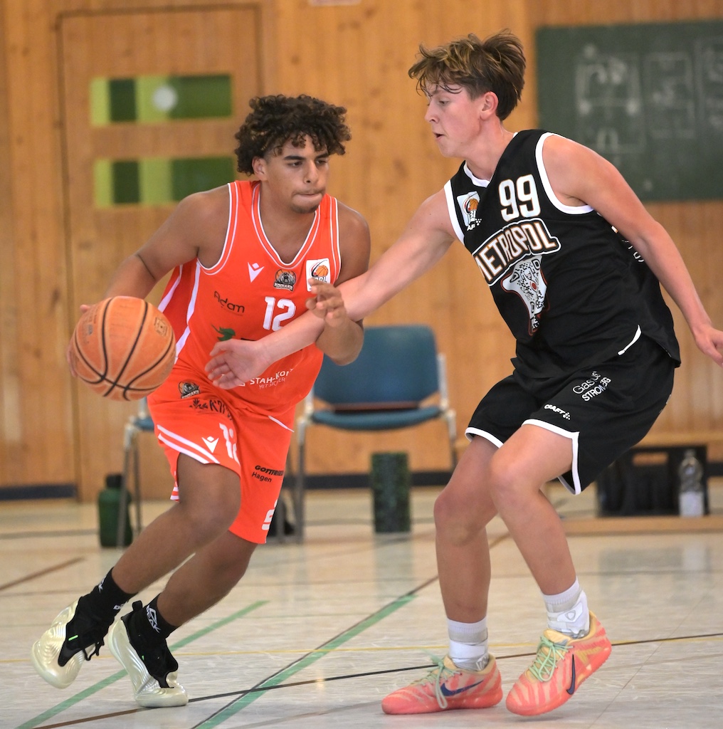 Zwei junge Basketballspieler in orangem und schwarzem Trikot im Zweikampf