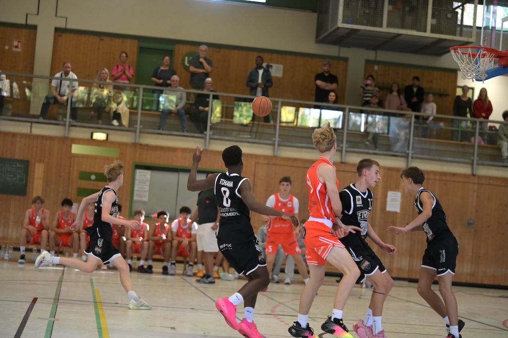 Junge Basketballspieler in schwarzen und orangenen Trikots beim Spiel in der Halle