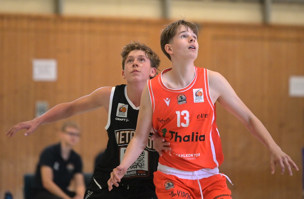 Zwei junge Basketballspieler in orangem und schwarzem Trikot kaempfen um Position