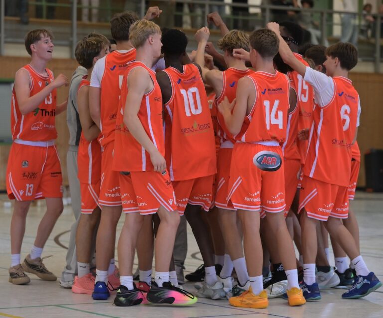 Ein Basketballteam in orangefarbenen Trikots versammelt sich motiviert in der Halle