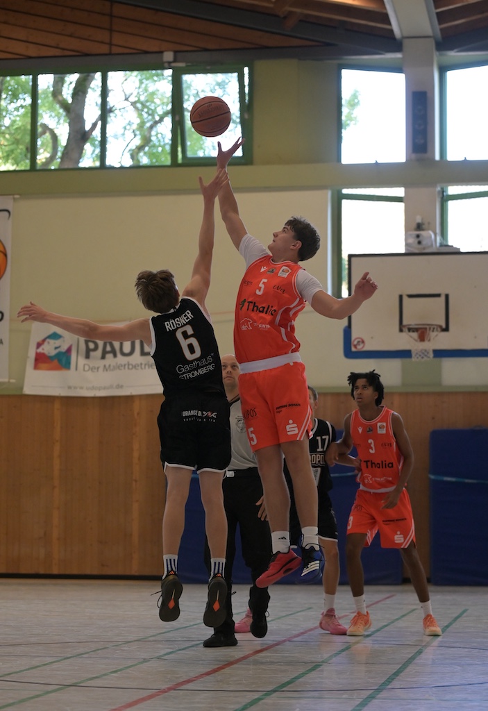 Zwei Basketballspieler in Orange und Schwarz springen konzentriert zum Ball